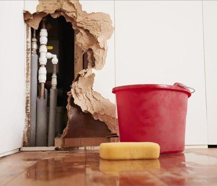 Hole in wall with red bucket on the floor.